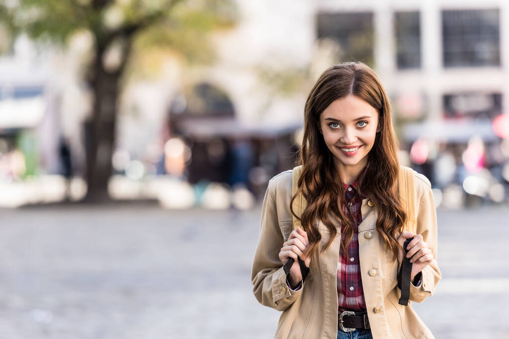 Menina bonita olhando para a câmera e sorrindo com mochila na cidade
 - Foto, Imagem