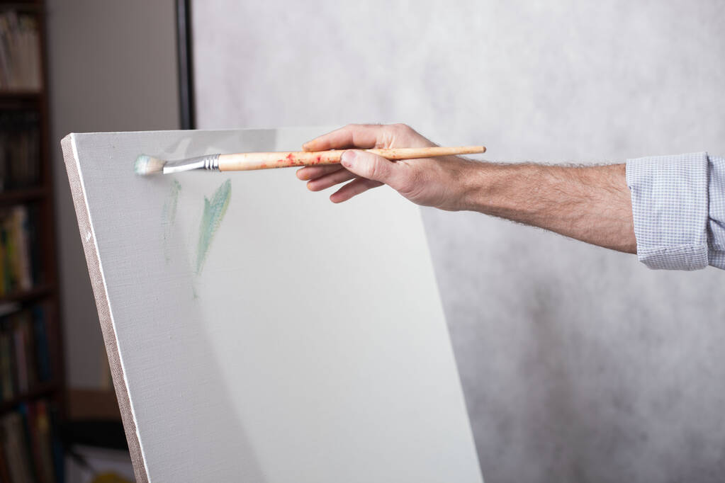 Beyaz bir tuval üzerinde fırça boyalarıyla sanatçı eli. Resimli bir resmin başlangıcı - Fotoğraf, Görsel