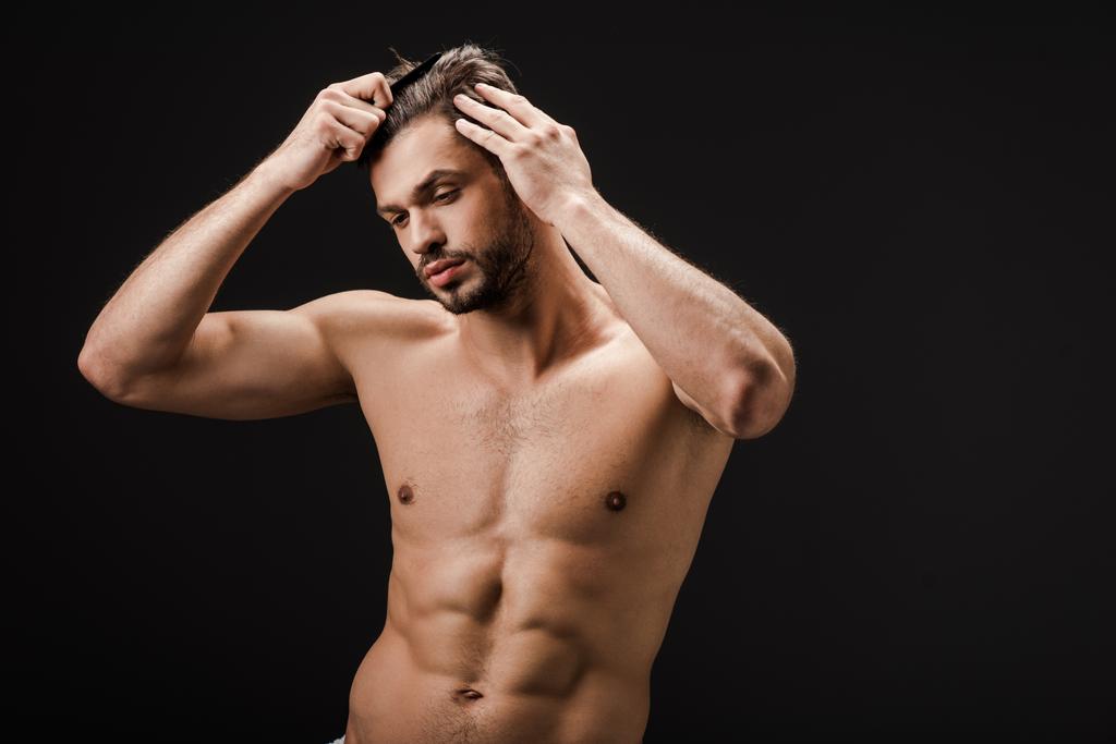 γενειοφόρος γυμνός άνδρας που χτενίζει τα μαλλιά του απομονωμένα σε μαύρο - Φωτογραφία, εικόνα
