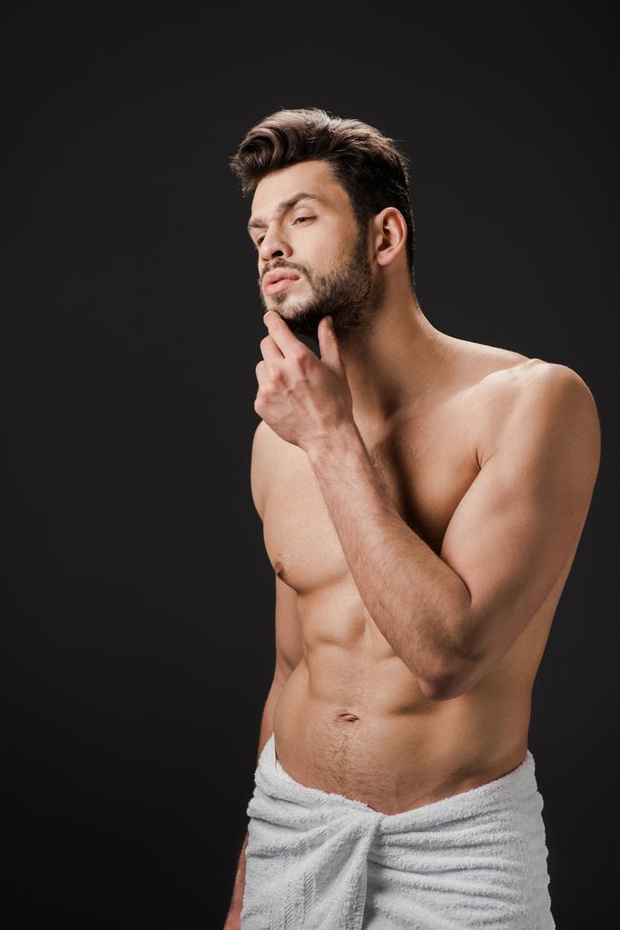 задумчивый сексуальный мужчина в полотенце касаясь бороды изолированы на черный
 - Фото, изображение