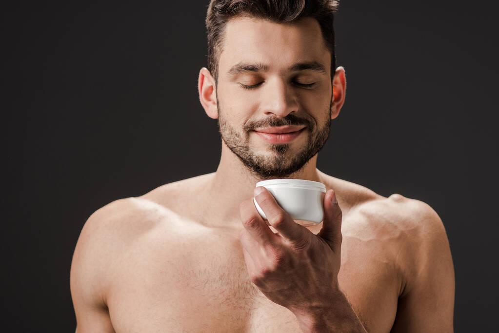 позитивний голий чоловік із закритими очима тримає пластиковий контейнер з кремом для обличчя ізольований на сірому
 - Фото, зображення