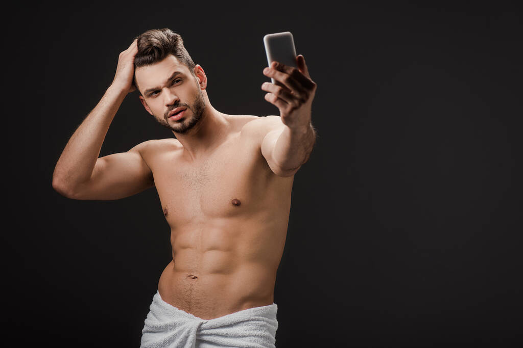 sexy man in towel taking selfie on smartphone isolated on black  - Photo, Image