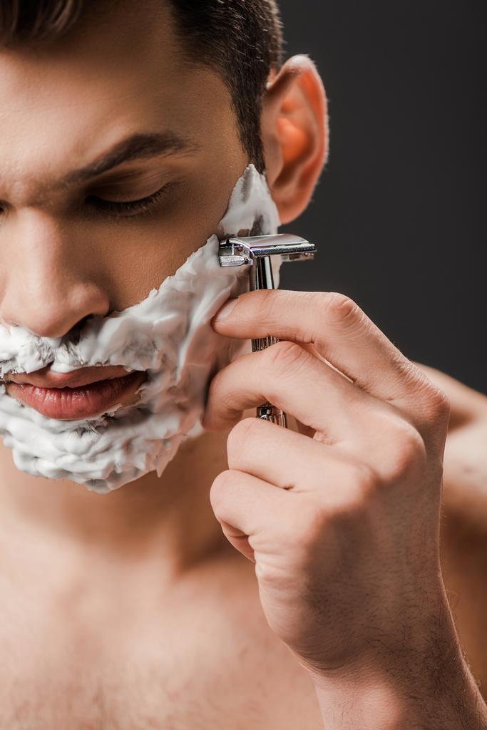 pohledný muž holení tvář s břitvou izolované na šedé - Fotografie, Obrázek