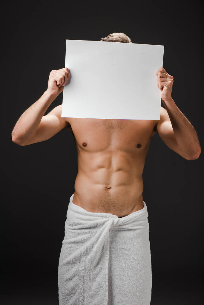 sexy uomo senza maglietta in asciugamano in possesso di cartello bianco davanti al viso isolato su nero
 - Foto, immagini