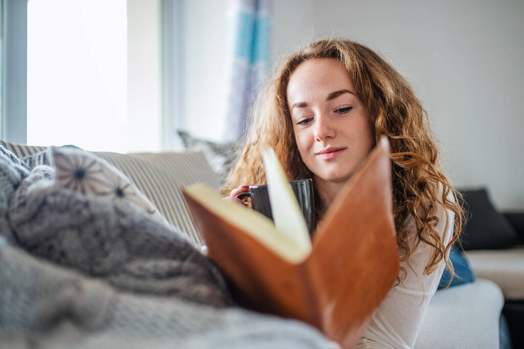 Jovem mulher relaxando dentro de casa com livro
. - Foto, Imagem