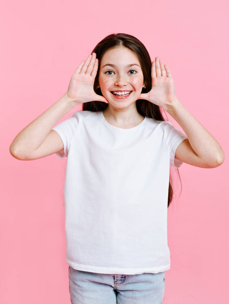 Retrato de adorable niña sonriente con la camiseta blanca divirtiéndose aislada sobre un fondo rosa
 - Foto, imagen