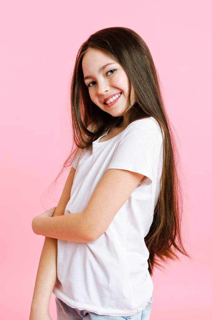Portrét roztomilé usměvavé holčičky v džínách a bílém tričku izolované na růžovém pozadí - Fotografie, Obrázek