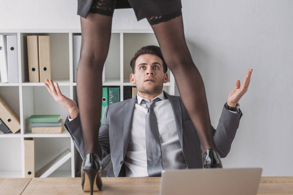 kivágott kilátás szexi titkárnő magas sarkú cipő áll az asztalon közelében megdöbbent üzletember - Fotó, kép