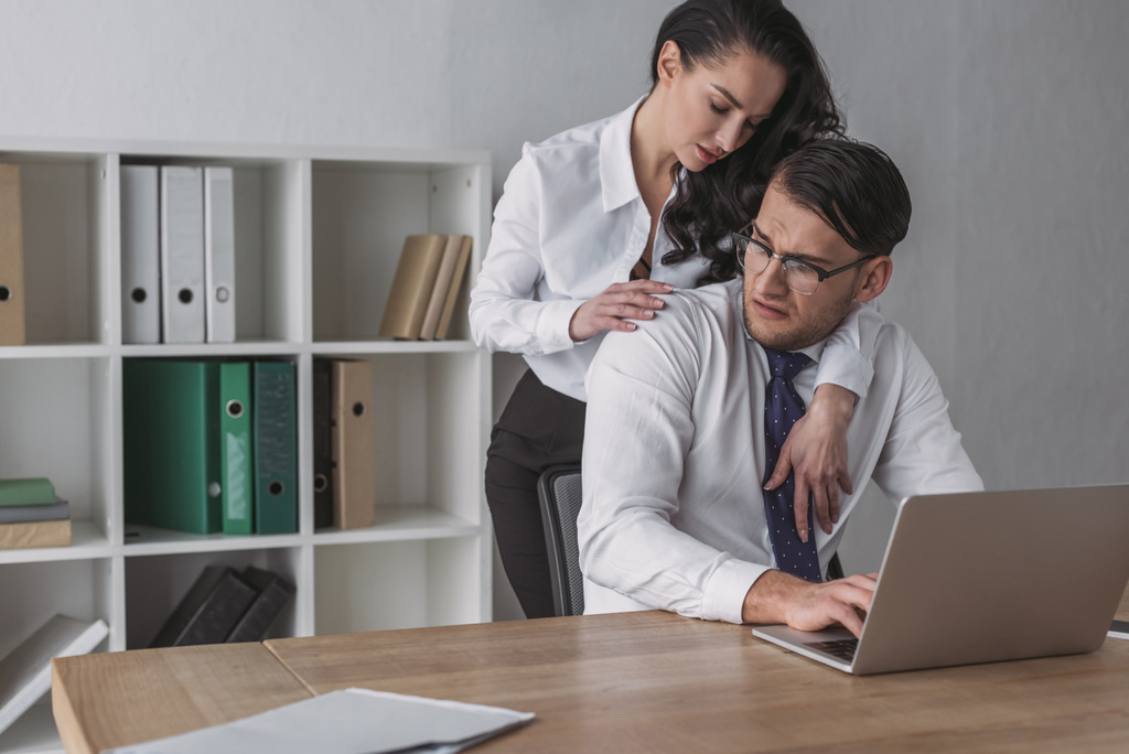 sexy businesswoman embracing confused colleague sitting at workplace - Photo, Image