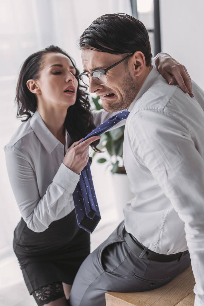 szexi titkárnő gazdaság nyakkendő és ölelés ijedt barátja, miközben elcsábítja őt az irodában - Fotó, kép