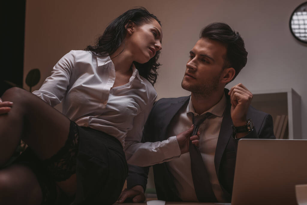 избирательный фокус сексуальной секретарши, сидящей на столе и трогающей галстук привлекательного бизнесмена
 - Фото, изображение