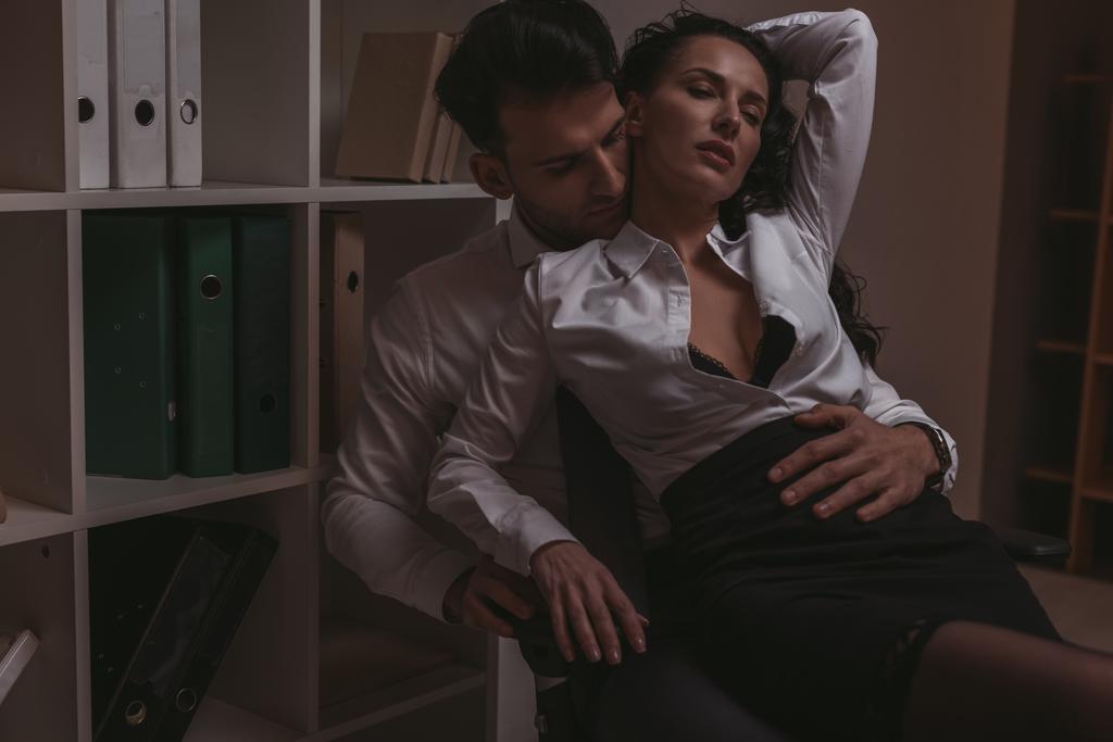 bonito empresário abraçando sensual secretário enquanto sentado no escritório cadeira juntos
 - Foto, Imagem