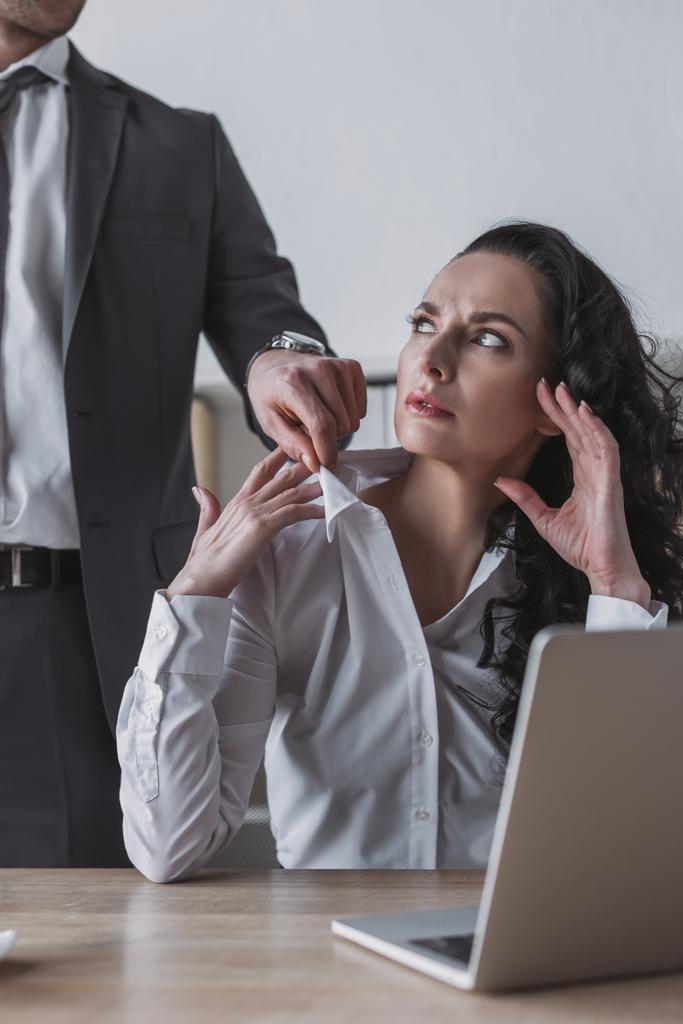 oříznutý pohled na obchodníka dotýkajícího se halenky rozzlobené sekretářky sedící na pracovišti - Fotografie, Obrázek
