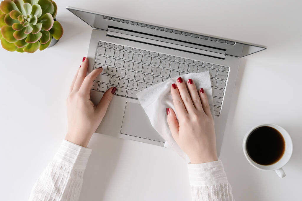 Una donna che pulisce con antivirus umido pulisce un computer portatile e una scrivania prima di iniziare a lavorare per proteggersi da batteri e virus
. - Foto, immagini