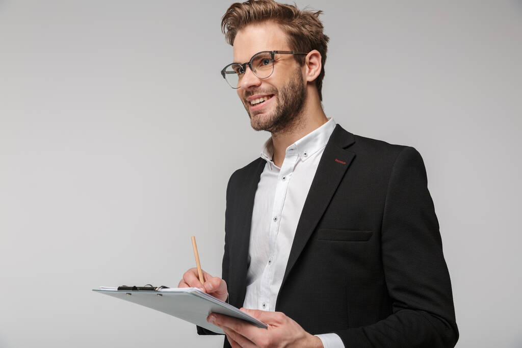 Портрет радісного молодого бізнесмена в окулярах, що тримає кишеню і посміхається ізольовано на білому тлі
 - Фото, зображення