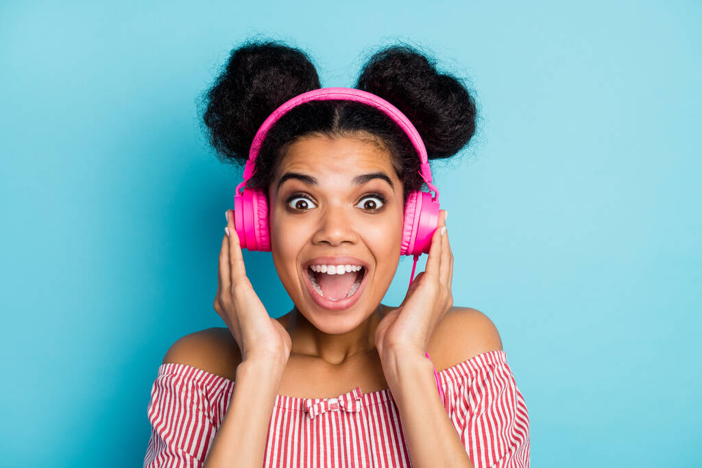 Lähikuva kuva hauska mukava tumma iho nainen kuunnella musiikkia moderni teknologia kuulokkeet auki suu suosikki laulu kulumista trendikäs punainen valkoinen raidallinen paita off-hartiat eristetty sininen väri tausta
 - Valokuva, kuva