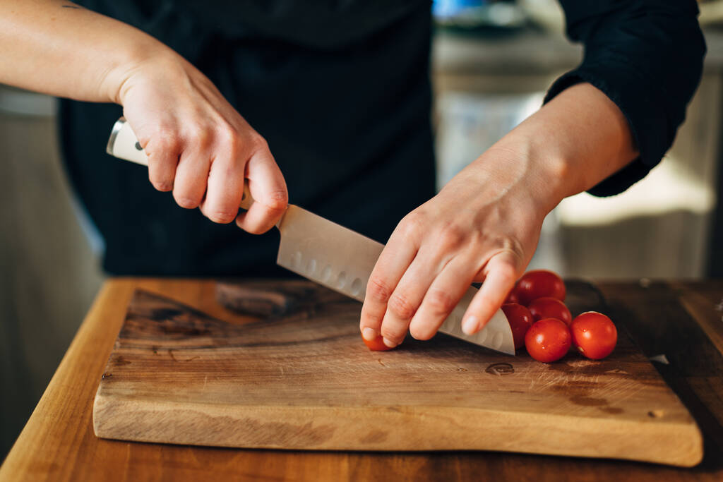 Chef hachant des tomates cerises au couteau sur une planche de bois
 - Photo, image