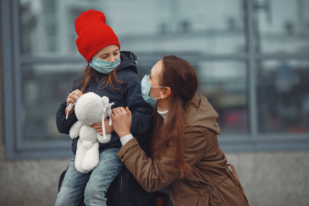 Una madre europea en un respirador con su hija está de pie cerca de un edificio.El padre le está enseñando a su hijo a usar máscara protectora para salvarse del virus. - Foto, imagen