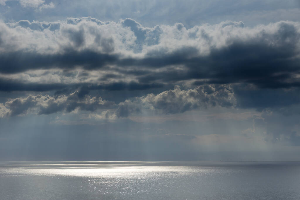 Mar Báltico en verano con sol en contraluz y nubes oscuras, Mar Báltico en verano con sol en contraluz y reflejos, puesta de sol ilumina ramas y piedras en agua de mar
 - Foto, Imagen