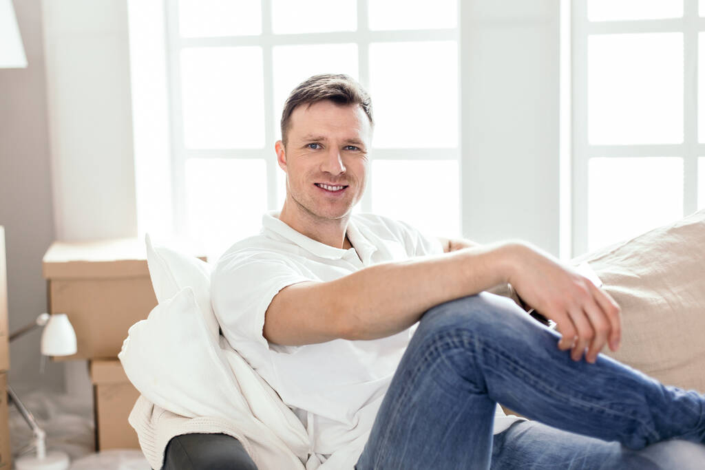 onnellinen mies istuu sohvalla uudessa asunnossaan
 - Valokuva, kuva
