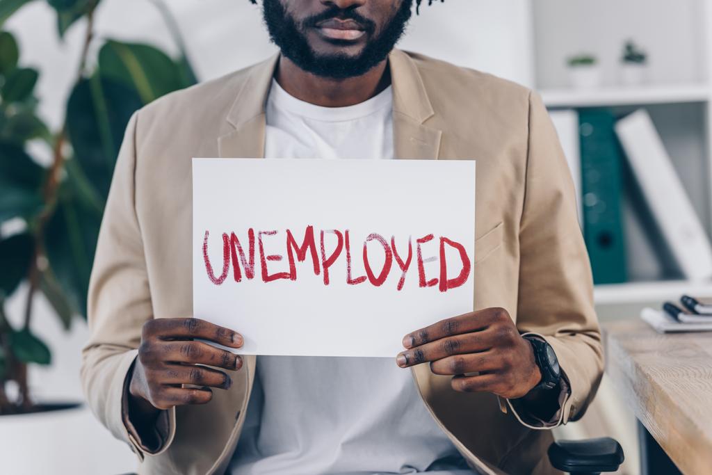 Vista ritagliata del dipendente afro-americano che mostra cartello con scritte disoccupate in ufficio
 - Foto, immagini