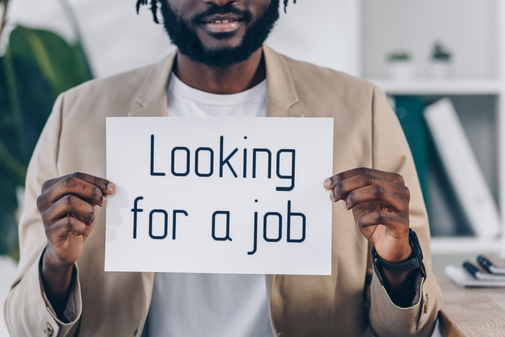 Обрезанный вид африканского американского работника, показывающего плакат с поиском работы с надписью в офисе
 - Фото, изображение
