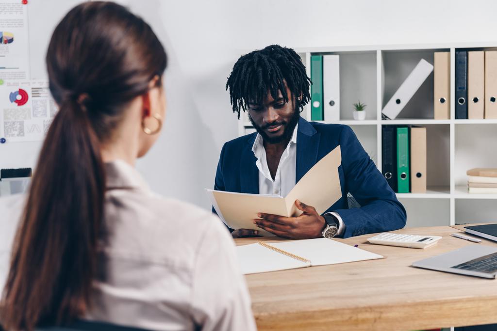 Enfoque selectivo del empleado y reclutador afroamericano con carpeta abierta en la mesa en la oficina
 - Foto, imagen