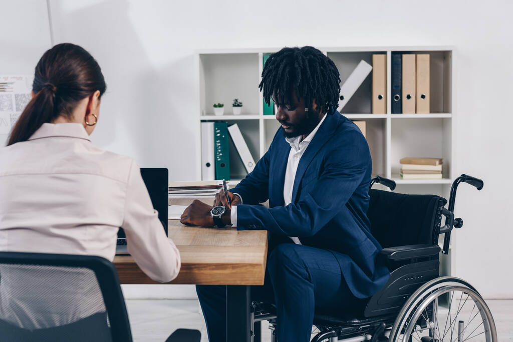 Afroamerykanin niepełnosprawny pracownik pisania blisko rekruter pracuje z laptopem w biurze - Zdjęcie, obraz