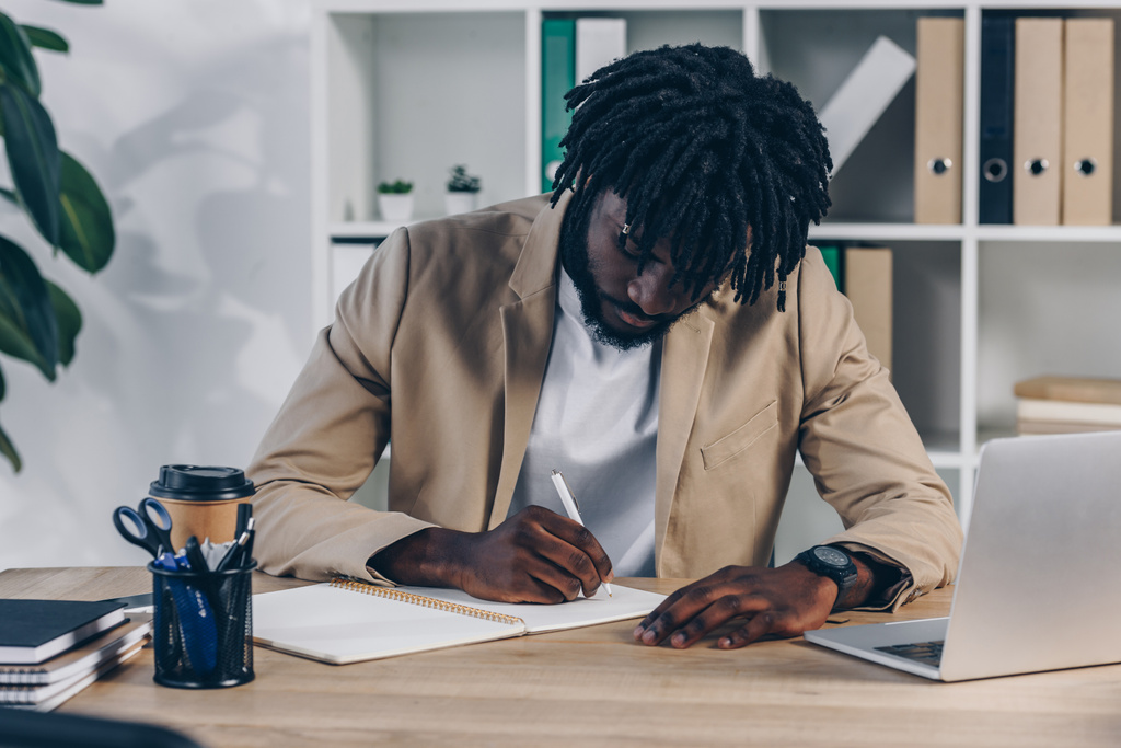 Afro-Amerikaanse recruiter gericht op het schrijven in notebook aan tafel in het kantoor - Foto, afbeelding