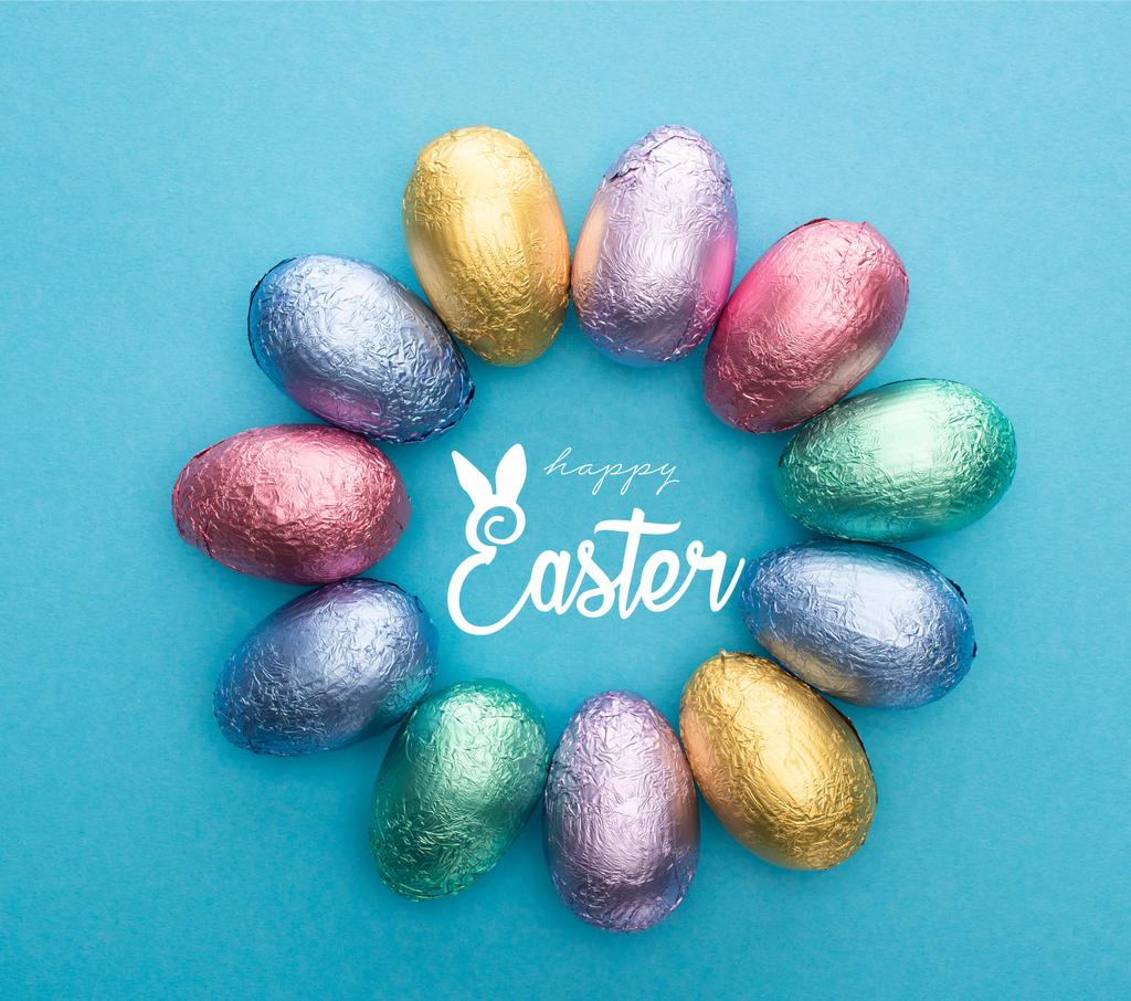 Vue du dessus du cercle avec des œufs de Pâques en chocolat dans une feuille colorée sur fond bleu avec une illustration de Pâques heureuse
 - Photo, image