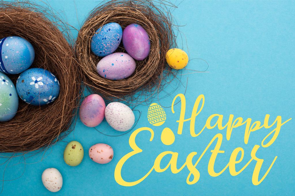 Top view of colorful Easter eggs in nests on blue background with happy Easter illustration - Photo, Image