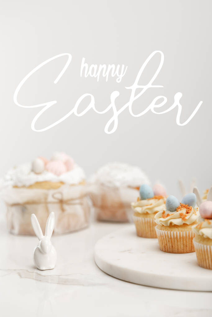 丸いボード上のカップケーキの選択的な焦点 幸せなイースターイラストとグレーの背景に装飾ウサギとイースターケーキ ロイヤリティフリー写真 画像素材