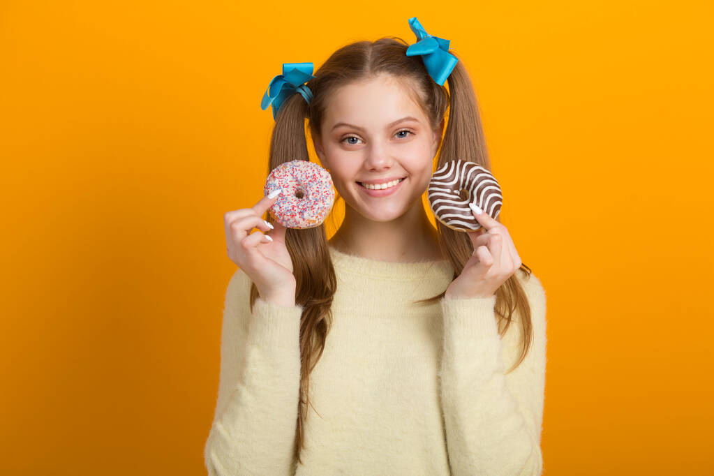 schöne junge Frau mit langen Haaren auf gelbem Hintergrund mit Donuts in den Händen - Foto, Bild