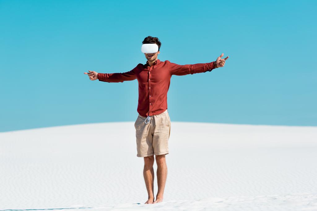 άνθρωπος στην αμμώδη παραλία σε vr ακουστικά με ανοιχτές αγκάλες κατά καθαρό γαλάζιο ουρανό - Φωτογραφία, εικόνα