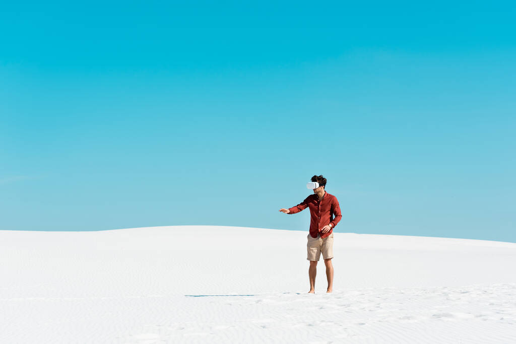 man on sandy beach in vr headset gesturing against clear blue sky - Photo, Image