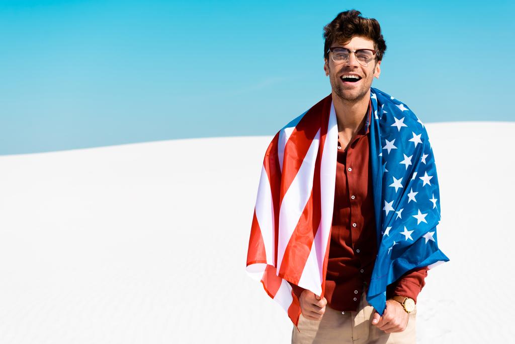 boldog jóképű férfi amerikai zászló homokos tengerparton ellen tiszta kék ég - Fotó, kép