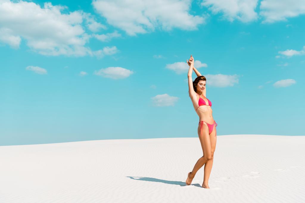 mooi sexy meisje in badpak met handen in de lucht op zandstrand met blauwe lucht en wolken - Foto, afbeelding