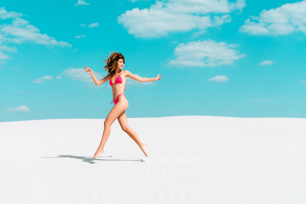 mooi sexy meisje in badpak springen op zandstrand met blauwe lucht en wolken - Foto, afbeelding