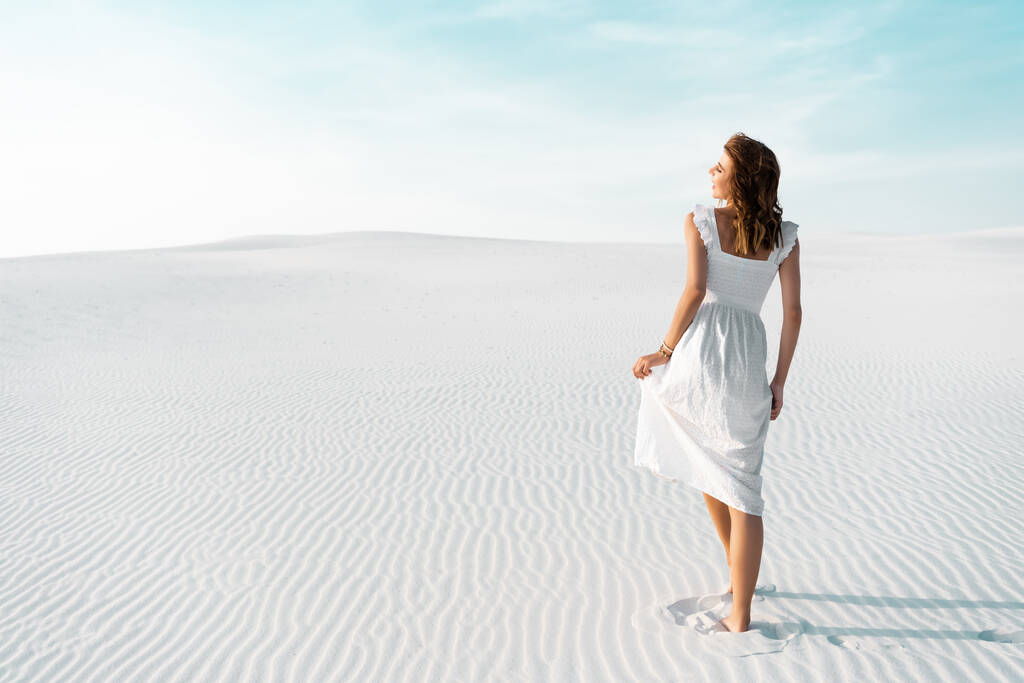 widok z tyłu piękna dziewczyna w białej sukience spacery po piaszczystej plaży z błękitnym niebem - Zdjęcie, obraz