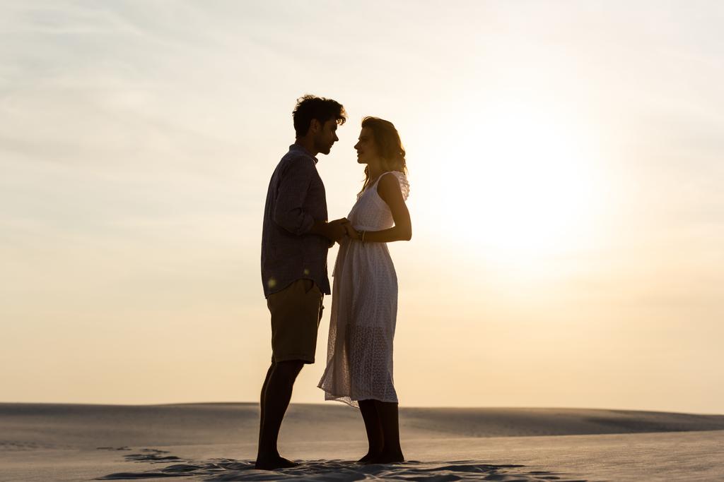夕暮れ時に砂浜で手をつないでいる若いカップルの側の景色 - 写真・画像
