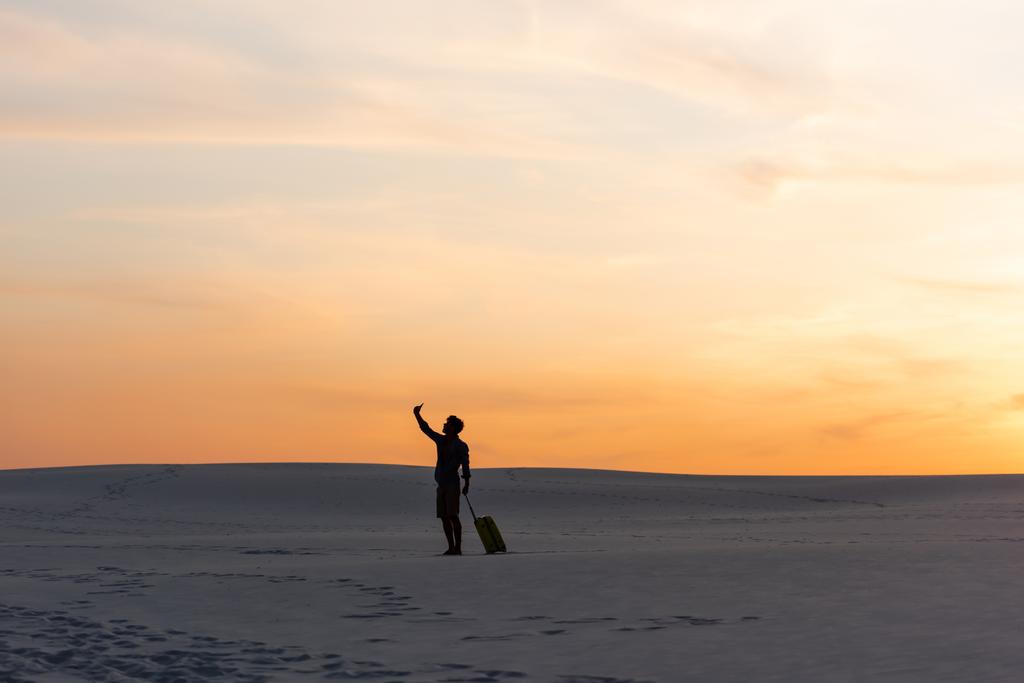 silhouette d'homme marchant sur la plage avec sac de voyage et smartphone au coucher du soleil
 - Photo, image