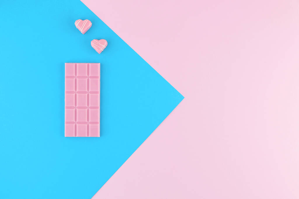 Ροζ σοκολάτα και καραμέλες σε σχήμα καρδιάς σε όμορφο ροζ και φωτεινό μπλε παστέλ φόντο. Φρέσκα γλυκά. Στο πάνω μέρος. Επίπεδη. Πρότυπο σχεδιασμού.  - Φωτογραφία, εικόνα