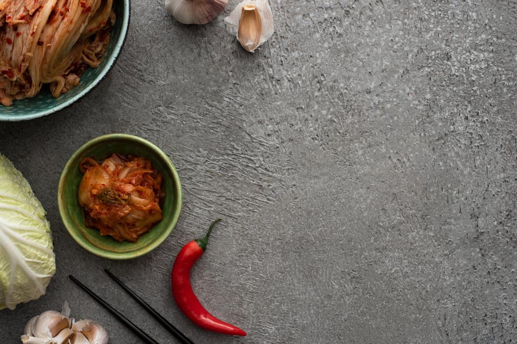 Beton yüzeyde kimchi, chili biber, sarımsak ve Çin lahanası olan kaselerin üst görüntüsü. - Fotoğraf, Görsel