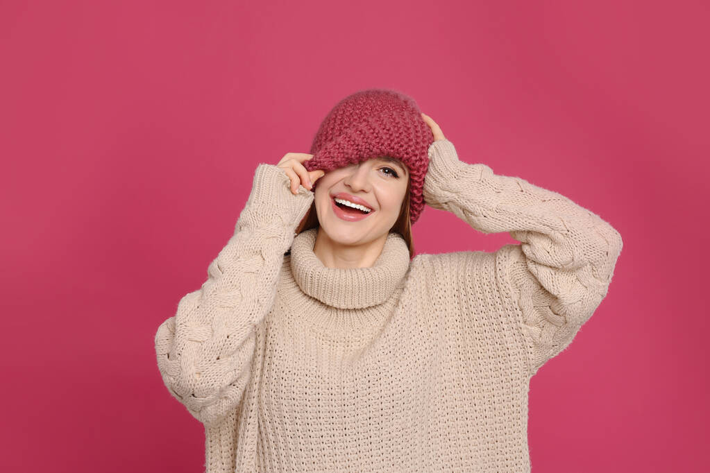 Młoda kobieta w ciepłym swetrze i kapeluszu na karmazynowym tle. Sezon zimowy - Zdjęcie, obraz