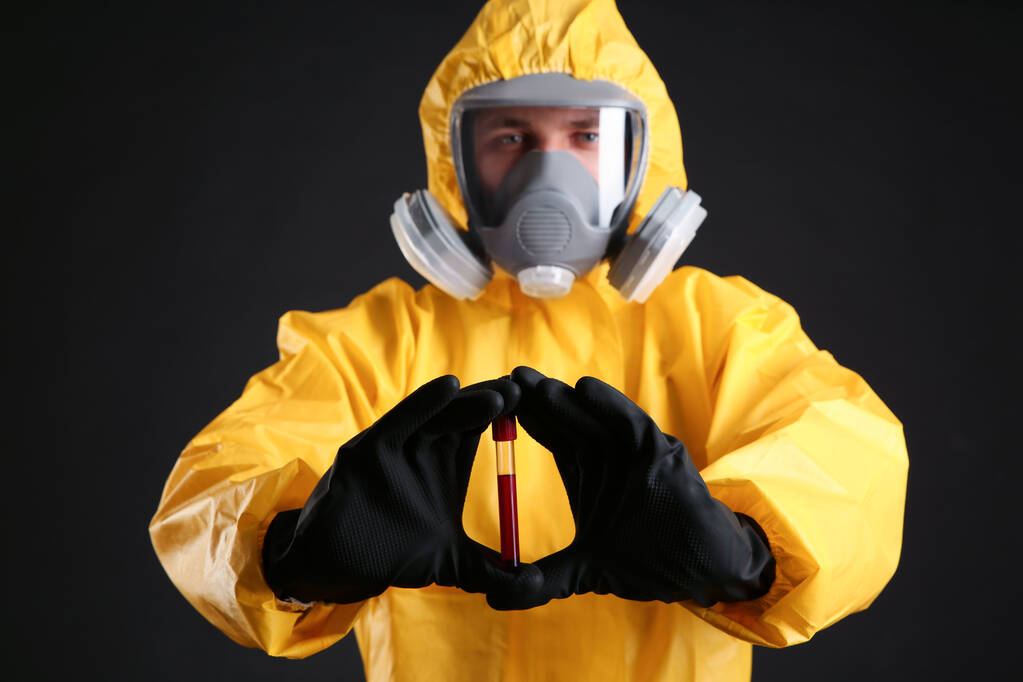 Muž v chemickém ochranném obleku drží zkumavku se vzorkem krve na černém pozadí. Virus research - Fotografie, Obrázek