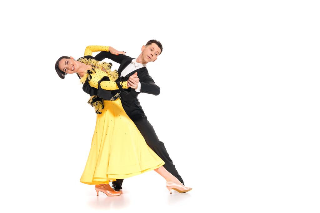 Улыбающаяся элегантная молодая пара танцовщиц в жёлтом платье и чёрном костюме танцующая на белом
 - Фото, изображение