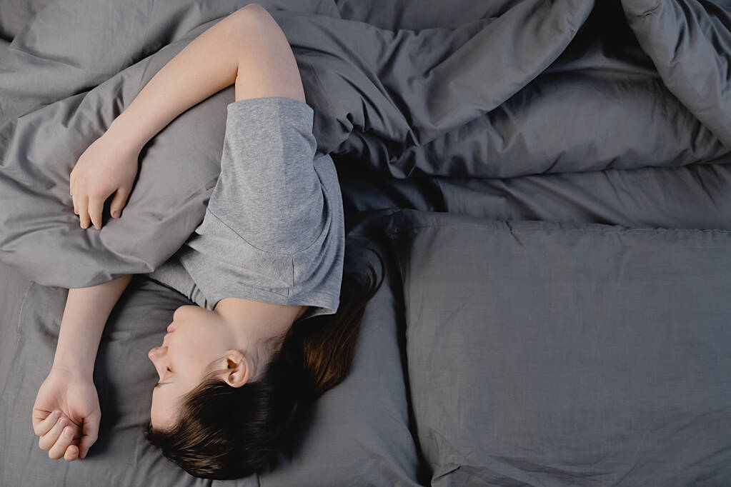 Draufsicht der ruhigen, brünetten Frau, die in einem bequemen Bett schläft, das auf einer orthopädischen Matratze mit weichem Kopfkissen liegt, friedliches junges Mädchen, das sich mit einer Decke auf grauen Laken im Schlafzimmer ausruht. - Foto, Bild