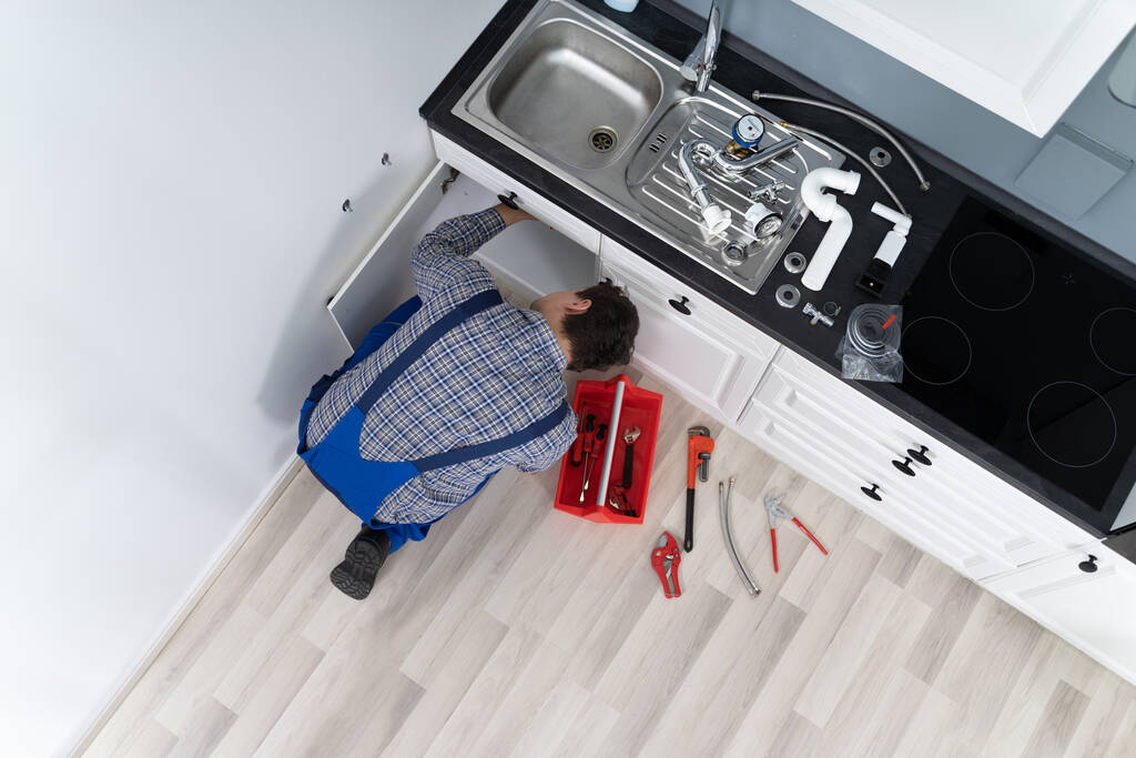 Lavoratore sdraiato sul pavimento che ripara il lavandino della cucina con la chiave regolabile
 - Foto, immagini