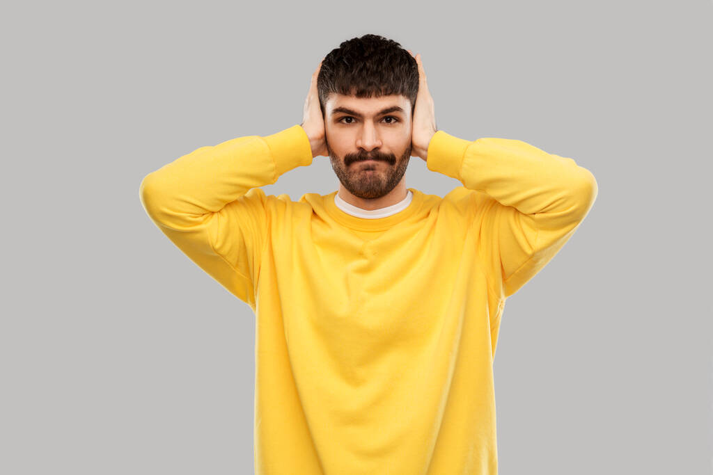 man in yellow sweatshirt closing ears by hands - 写真・画像