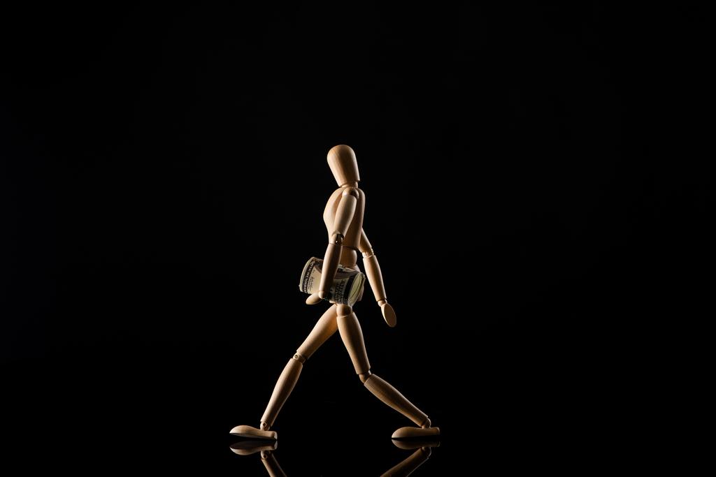 Boneca de madeira imitando andando com dinheiro em fundo preto
 - Foto, Imagem